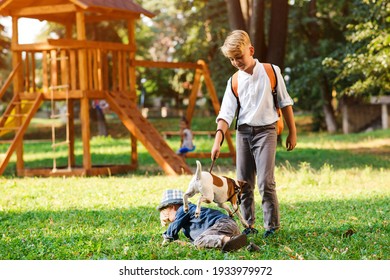 Children With Dog Walking In The Park. Family, Friendship, Animals And Lifestyle. Kids With Jack Russel Terrier Dog Outdoors. Happy Boys Playing With Dog On Green Grass.