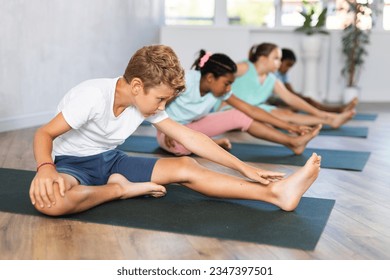 Children doing yoga training, sitting in Janu Sirsasana, head-to-knee forward bend pose, asana for strengthening and stretching shoulders, spine, groins, and hamstrings. - Powered by Shutterstock