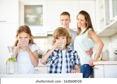 Children Drink Fresh Water With Limes In The Kitchen In Front Of Their Parents