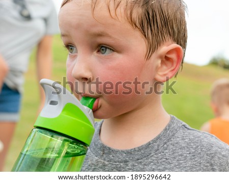 Children drinking water. A thirsty boy taking a water break after playing outdoor.