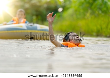 Children drowning water the river and blowing whistle show sign for helping and save life, danger for kids playing and swimming water in summer season but safty by life vest, blurred people and boat 