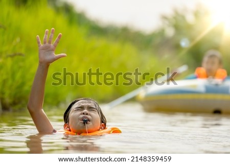 Children drowning water the river and blowing whistle show sign for helping and save life, danger for kids playing and swimming water in summer season but safty by life vest, blurred people and boat 