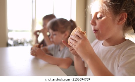 Children Eat Burgers. Fast Food Burger. Fun A Group Of Small Children In The Kitchen Greedily Eat Fast Food Burgers. Big Family Small Kids Having Breakfast In The Morning In The Kitchen Eating Burger