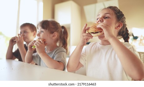 Children Eat Burgers. Fast Food Burger. A Group Fun Of Small Children In The Kitchen Greedily Eat Fast Food Burgers. Big Family Small Kids Having Breakfast In The Morning In The Kitchen Eating Burger