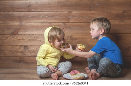 Children Eating Donuts. Happy Boy And Girl Sitting On The Floor And Having Fun With Doughnut. Tasty Food For Kids. Happy Time At Home With Sweet Food. Share Food