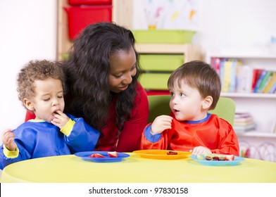 Children eating fruit at a nursery as their carer watches on - Powered by Shutterstock