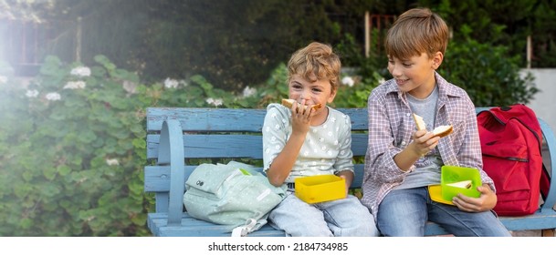 Children eating lunch sandwiches in school yard during break, sitting on the bench. Share the food, talking, laughing, resting outdoor. Back to school routine. 4K - Powered by Shutterstock