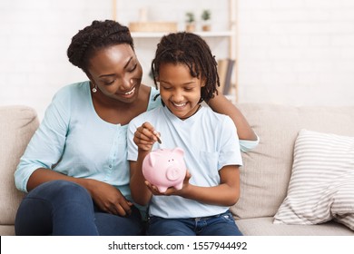 Children And Economy. Little African American Girl Putting Coin In Piggybank, Saving Money.