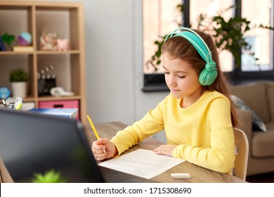 children, education and distant learning concept - student girl in headphones doing school test at home