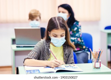 Children With Face Mask Back To School In Classroom After Covid-19 Lockdown - Teacher Helping Kid To Use Computer Doing Hybrid Education Class After School Reopening