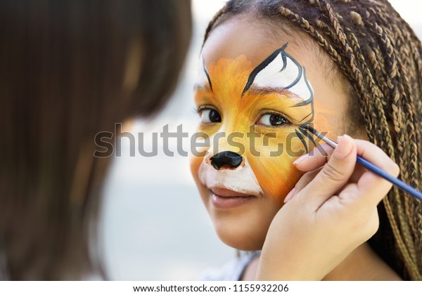 Children face painting. Artist painting\
little african-american girl like tiger, copy\
space