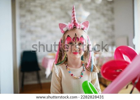 Children face painting. Little preschooler girl in unicorn costume with facepaint on a birthday party. Creative activities for kids