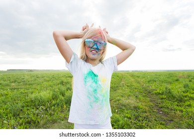 Children, festival of holi and holidays concept - happy little girl covered with color powder smiling over nature background
