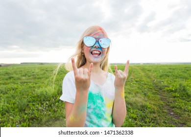 Children, festival of holi and holidays concept - happy little girl wearing sunglasses covered with color powder smiling over nature background