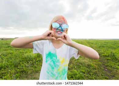 Children, festival of holi and holidays concept - happy little girl covered with color powder smiling over nature background