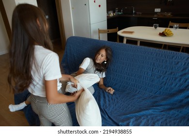 Children Fight With Pillows On The Sofa, Two Sisters Play On The Sofa With Pillows, Run Around The Apartment. Mom Keeps Calm. Mother Of The Year