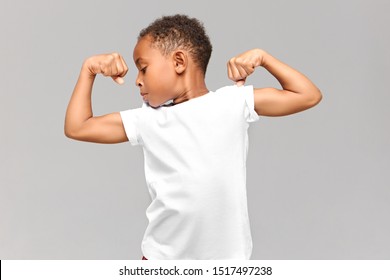 Children, fitness and bodybuilder concept. Studio shot of athletic muscled African American boy in casual t-shirt demonstrating strength by tensing bicep muscles, having proud confident look - Powered by Shutterstock