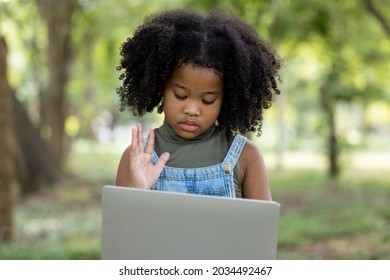 Children Girl African American Ethnicity Black Skin Sitting On Tree Base Use Laptop Computer Via Video Call And Holding Hands Goodbye Friends And She Looks Sad With 5G Internet Signal In The Park,