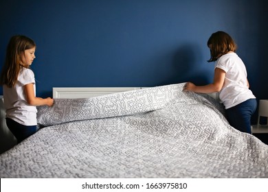 Children Girls Sisters Cover The Bed With A Bedspread, Children Help With Housework, Children Make The Bed. Bright Bedroom With Blue Wall And Bedding