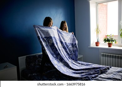 Children Girls Sisters Cover The Bed With A Bedspread, Children Help With Housework, Children Make The Bed. Bright Bedroom With Blue Wall And Bedding