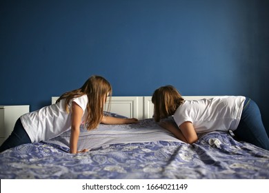 Children Girls Sisters Cover The Bed With A Bedspread, Children Help With Housework, Children Make The Bed. Bright Bedroom With Blue Wall And Bedding