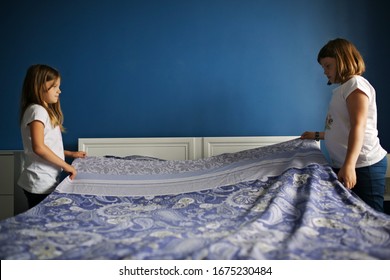 Children Girls Sisters Cover The Bed With A Bedspread, Children Help With Housework, Children Make The Bed. Bright Bedroom With Blue Wall And Bedding