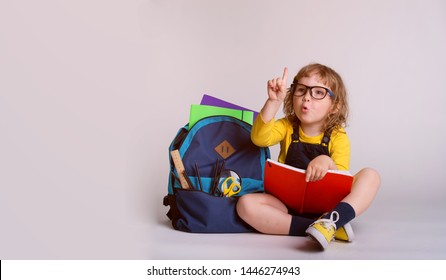 Children Go Back To School. Little Happy  Girl Doing Homework At Home With Backpack Full Of Books, Pencils. Pupil Reading A Book, Writing And Painting.  Kid Is Drawing. Child In Glasses. 