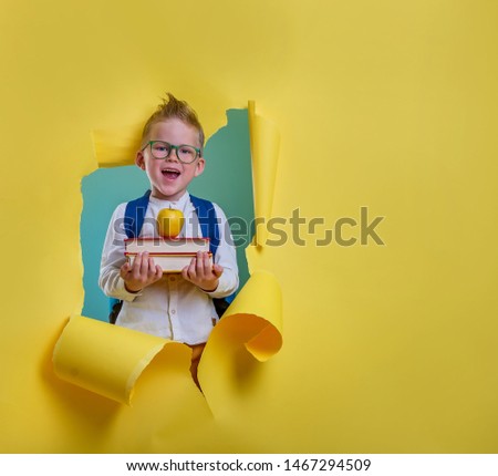 Children go back to school. Pupil of primary school with backpack and book breaking yellow paper wall. Beginning of lessons. First day of fall. Elementary student.