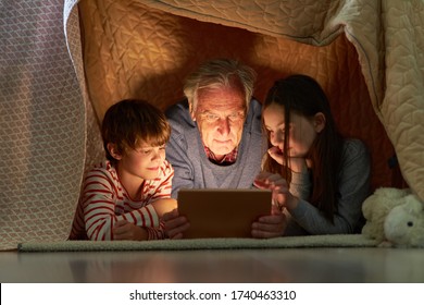 Children and grandfather using tablet computer or e-book under a blanket as a tent - Powered by Shutterstock