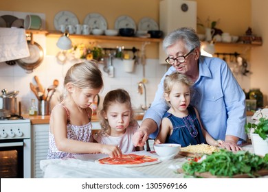 Children And Grandmother Cooking Italian Pizza In Cozy Home Kitchen For Family Dinner. Cute Kids Girls Are Preparing Homemade Food. Three Little Sisters Are Helping Old Senior Woman. Lifestyle Moment.