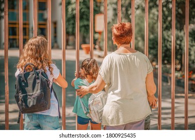 Children With Grandmother Wait Outisde A Closed School Gate. Back To School In The Time Of Covid 19.