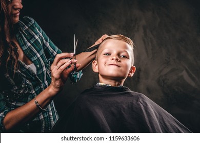 Children hairdresser with scissors is cutting little boy against a dark background. Contented cute preschooler boy getting the haircut.  - Powered by Shutterstock