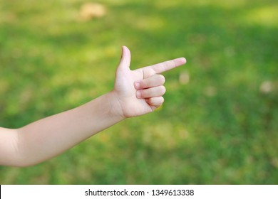 Children Hand Pointing With Index Finger Or Making Gun Gesture On Blur Green Garden Background. Kid Hand Show Up Forefinger Correct Or Point.