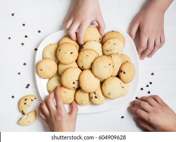 Children Hands Holding American Homemade Cookies With Chocolate Drops In White Plate On Table. Top View, Sharing Food Concept.