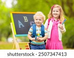 Children happy to be back to school. Preschooler girl and boy with backpack and books at black chalk board learning to write letters and read. Kids at preschool or kindergarten learn the alphabet.