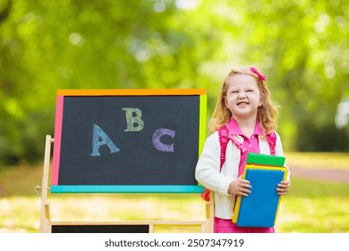 Children happy to be back to school. Preschooler girl and boy with backpack and books at black chalk board learning to write letters and read. Kids at preschool or kindergarten learn the alphabet. - Powered by Shutterstock