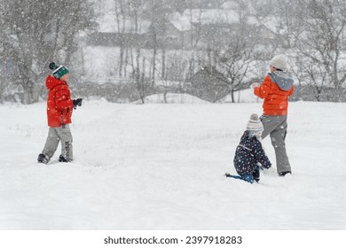 Children have fun outside in the winter during snowfall. Kids play snowballs. Winter entertainment