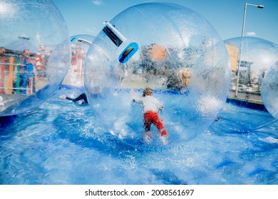 Children have fun, rolling around inside giant plastic zorbing balloons floating on water