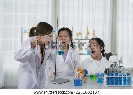 children having fun doing chemistry experiments in the science classroom that chemical laboratory staff as a mentor teaching kids test the liquid in a flask