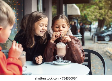 Children Having Fun In Outdoor Cafe. Kids Talking And Drinking Cocoa For The Breakfast In The City Street In Autumn. Spending Weekend With Friends.