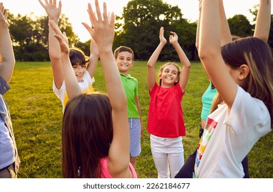 Children having fun in the park. Happy kids playing all together. Group of cheerful, excited friends standing on a green meadow, raising their hands up and smiling. Summer break and friendship concept - Shutterstock ID 2262184677