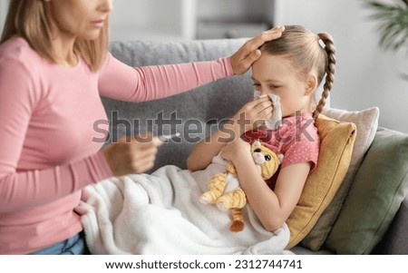 Children Healthcare. Mother checking temperature of her sick little daughter at home, caring mom looking at thermometer in hand and touching forehead of ill female child, closeup shot