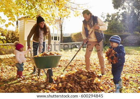 Children Helping Parents To Collect Autumn Leaves In Garden