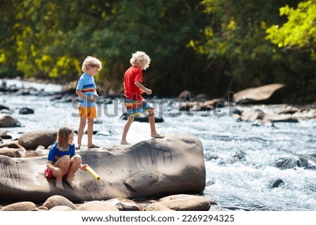 Children hiking in Alps mountains crossing river. Kids play in water at mountain in Austria. Spring family vacation. Little boy and girl on hike trail. Outdoor fun. Active recreation with children.