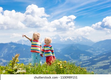 Children Hiking In Alps Mountains. Kids Look At Snow Covered Mountain In Austria. Spring Family Vacation. Little Boys On Hike Trail In Blooming Alpine Meadow. Outdoor Fun And Healthy Activity.

