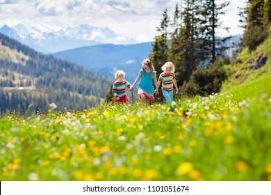 Children Hiking In Alps Mountains. Kids Run At Snow Covered Mountain In Austria. Spring Family Vacation. Little Boy And Girl On Hike Trail In Blooming Alpine Meadow. Outdoor Fun And Healthy Activity.
