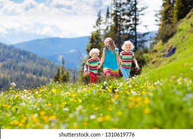 Children Hiking In Alps Mountains. Kids Run At Snow Covered Mountain In Austria. Spring Family Vacation. Little Boy And Girl On Hike Trail In Blooming Alpine Meadow. Outdoor Fun And Healthy Activity.
