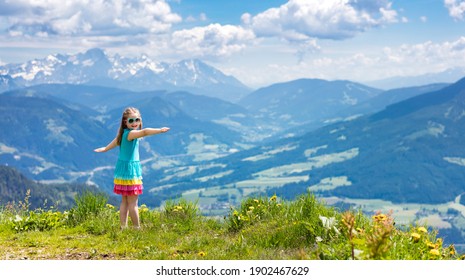 Children Hiking In Alps Mountains. Kids Look At Snow Covered Mountain In Austria. Spring Family Vacation. Little Girl On Hike Trail In Blooming Alpine Meadow. Outdoor Fun And Healthy Activity.

