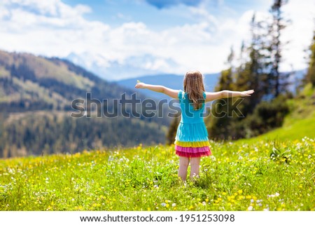Children hiking in Alps mountains. Kids look at snow covered mountain in Austria. Spring family vacation. Little girl on hike trail in blooming alpine meadow. Outdoor fun and healthy activity.

