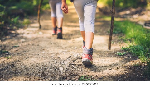 Children hiking in mountains or forest with sport hiking shoes. Girls or boys are walking trough forest path wearing mountain boots and walking sticks. Frog perspective with focus on the shoes.